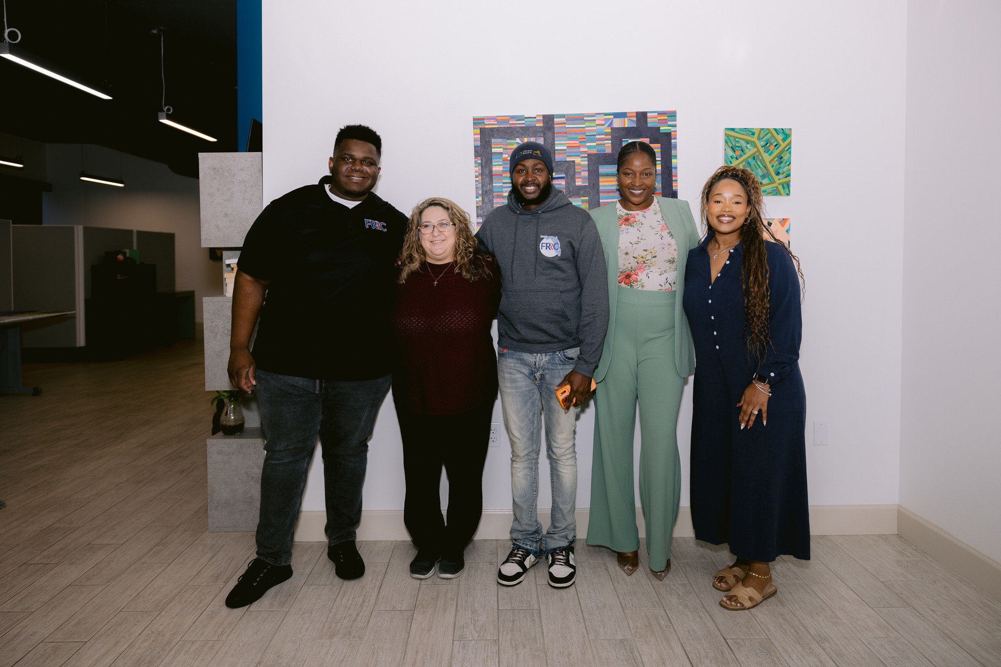 - Innocence Project of Florida Five people of diverse backgrounds pose together indoors, smiling at the camera with colorful art on the wall behind them.